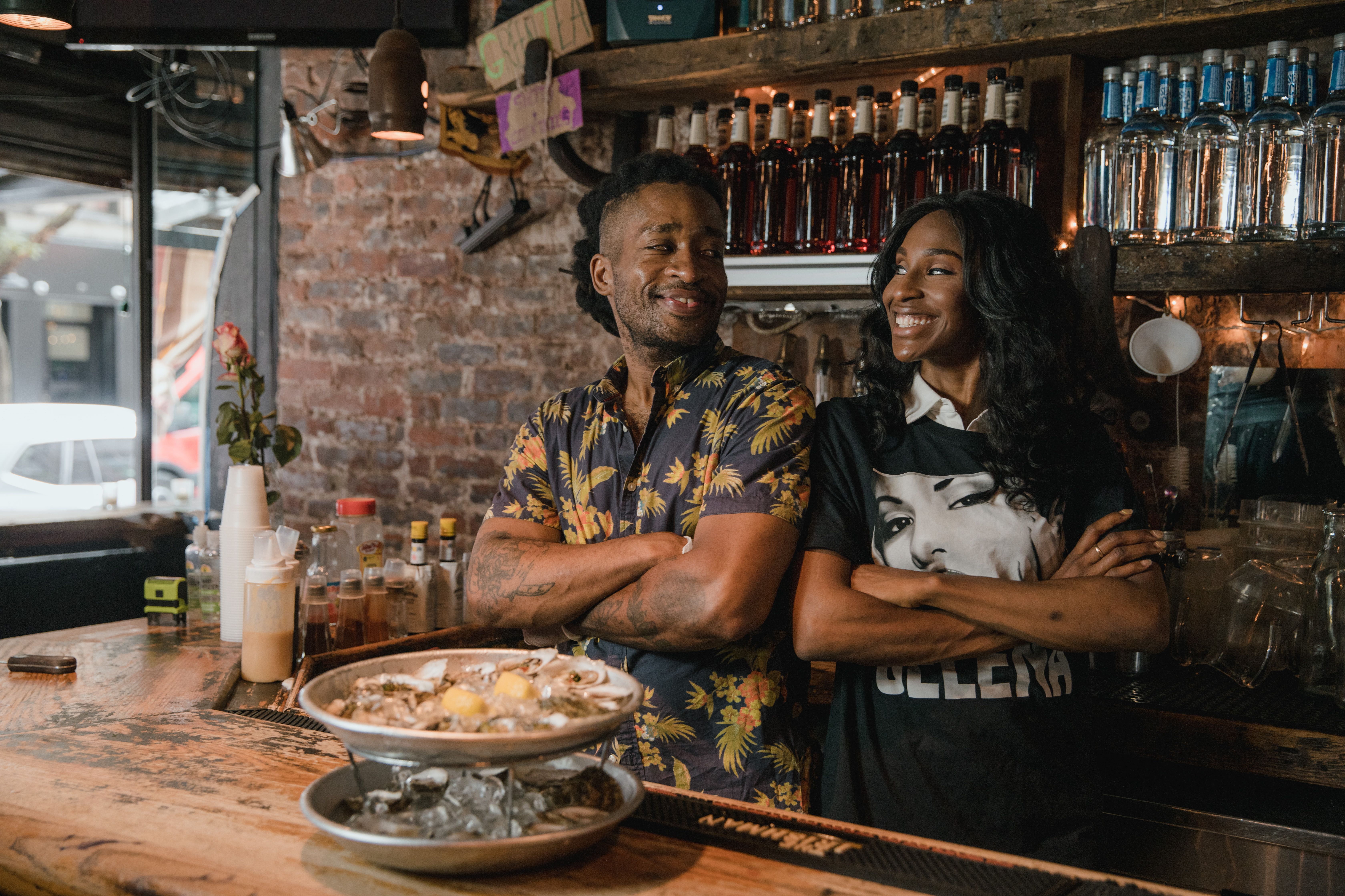 Two Black small-business owners standing together behind the counter of their neighborhood restaurant
